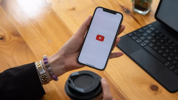 mão que segura um celular que mostra na tela o ícone do youtube. banner vídeo imobiliário sem verba